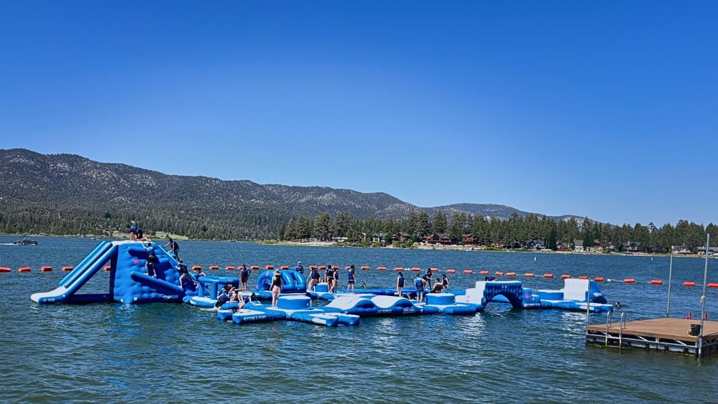 Visitors enjoying the floating inflatable water park on Big Bear Lake with scenic mountain views.