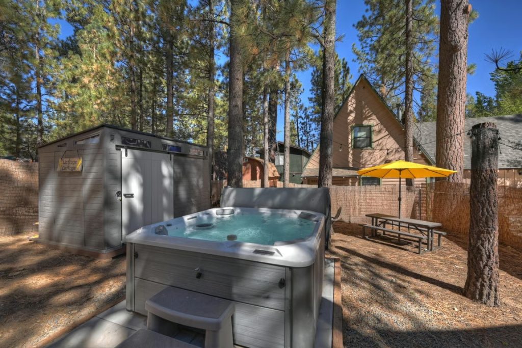 Big Bear cabin with an outdoor hot tub, picnic table, yellow umbrella, and tall pine trees