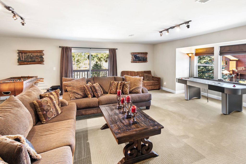 A cozy, rustic cabin game room in Big Bear with a foosball table, a pool table, and a brown sectional sofa.