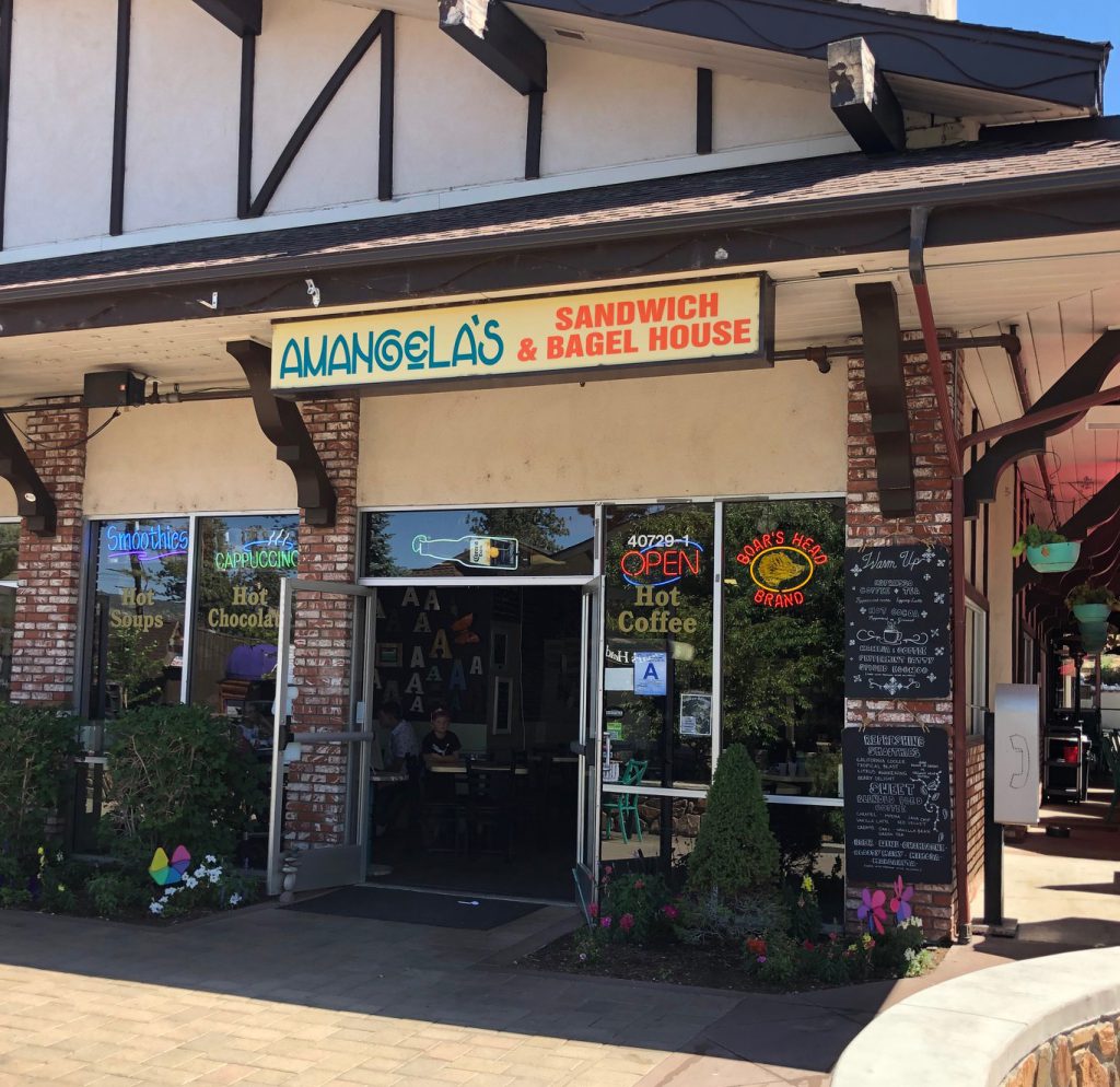 The front entrance of a cafe with a sign that reads "Amangela's Sandwich & Bagel House" in a brick and timber-framed building in Big Bear.