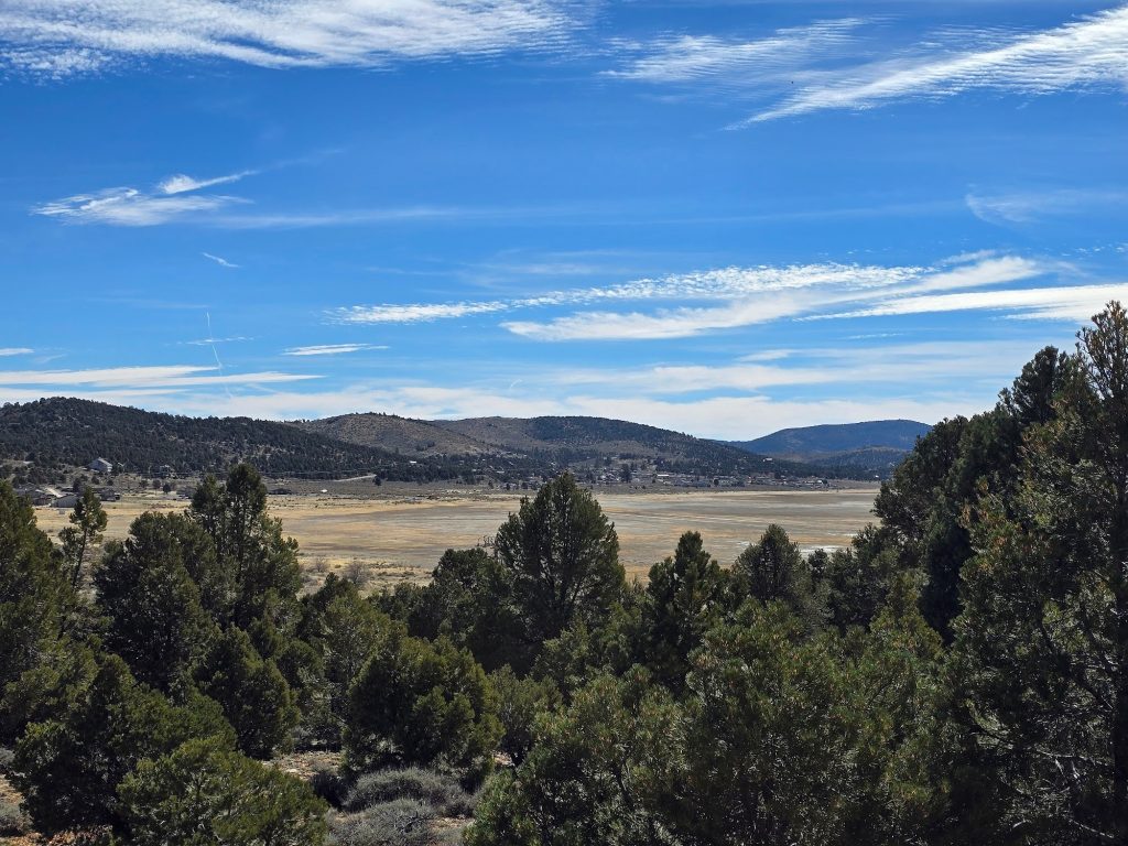 Winter view of Baldwin Lake Ecological Reserve with sagebrush, scattered snow patches, open meadow, and mountains beneath dramatic clouds.