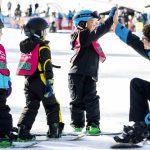 A group of children skiing and snowboarding on a snowy slope at Big Bear Lake.