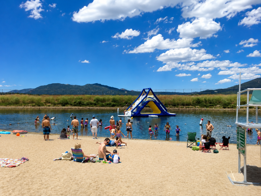 Families enjoying sandy swim beach at Big Bear Lake with inflatable water park, swimming area, and summer recreation activities