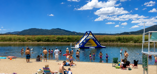 Families enjoying sandy swim beach at Big Bear Lake with inflatable water park, swimming area, and summer recreation activities