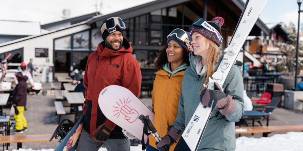 Three friends with snowboards and skis smile in the snowy setting of Big Bear