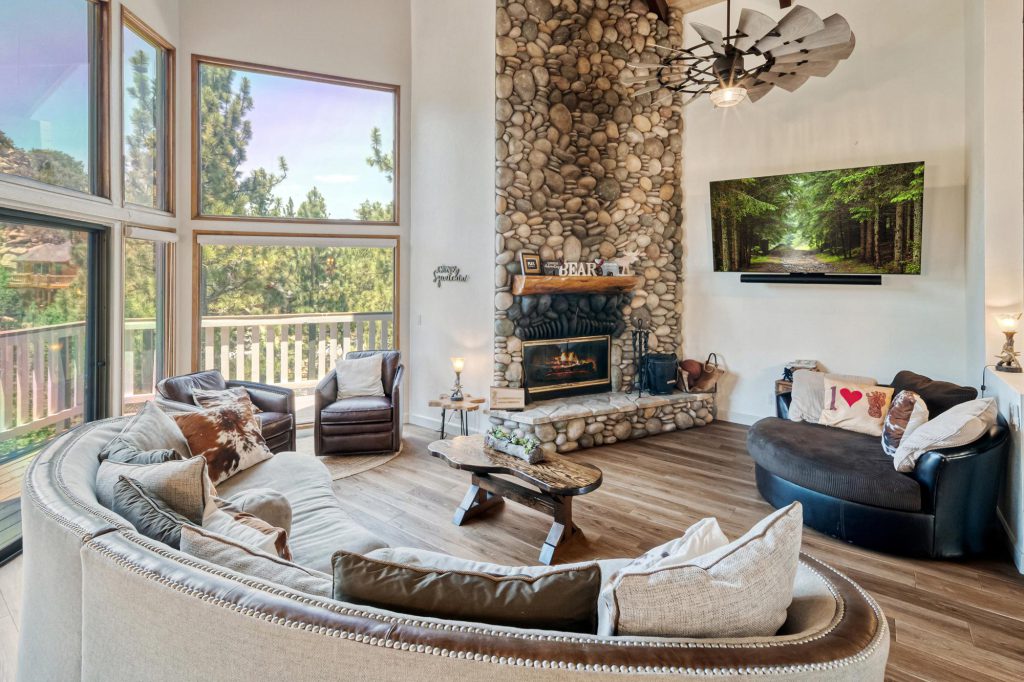 A cozy living room in the Bigfoot cabin, featuring a stone fireplace and large windows letting in natural light.