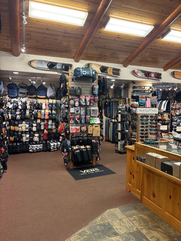 Inside Blauer Board Shop displaying winter gloves, backpacks, sunglasses, and snowboard accessories in Big Bear Lake.