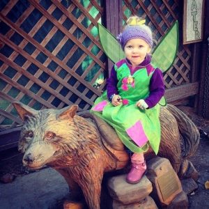 Child dressed in a fairy costume sitting on a wolf statue during Boo at The Zoo event