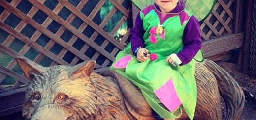 Child dressed in a fairy costume sitting on a wolf statue during Boo at The Zoo event