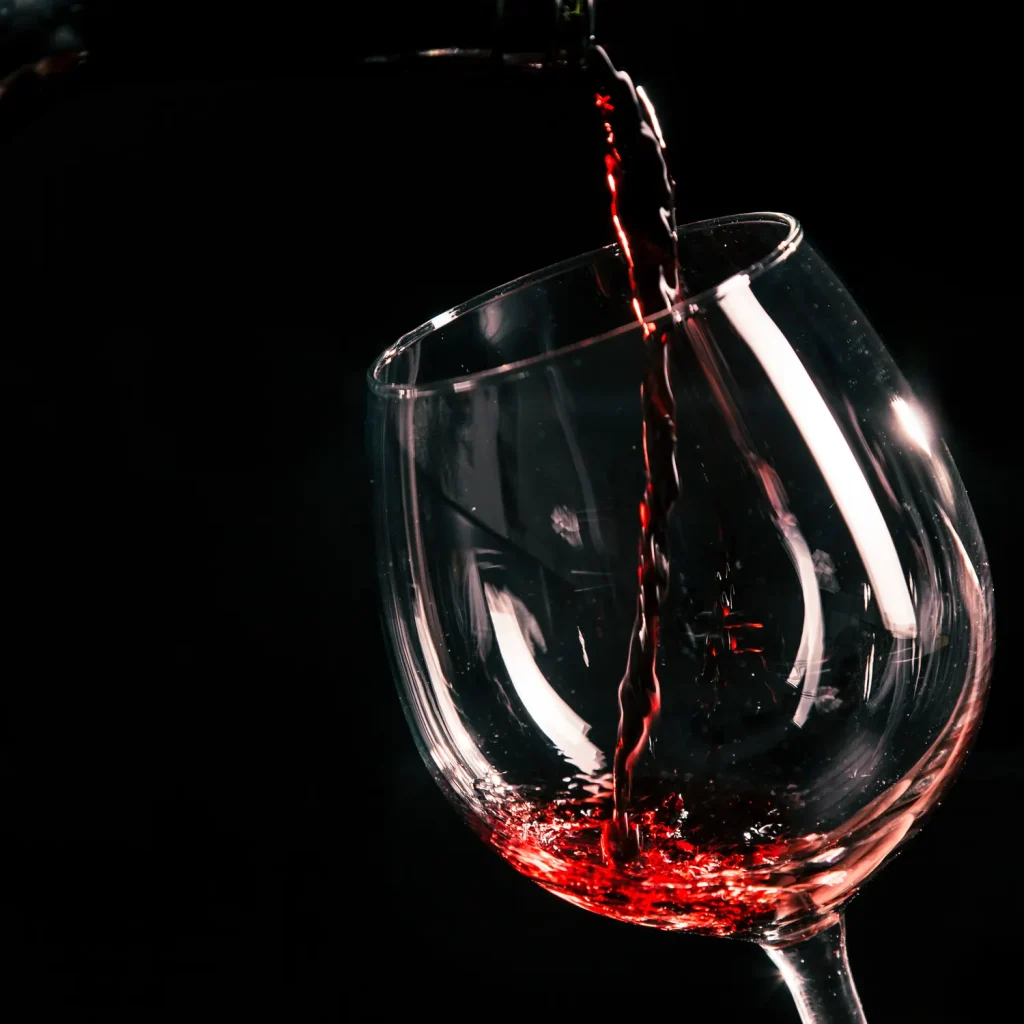 A stream of red wine is being poured into a clear wine glass against a dark background at Big Bear