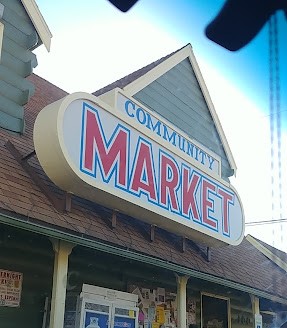 A large sign with "Community Market" in red and blue letters hangs from the front of a small market building.