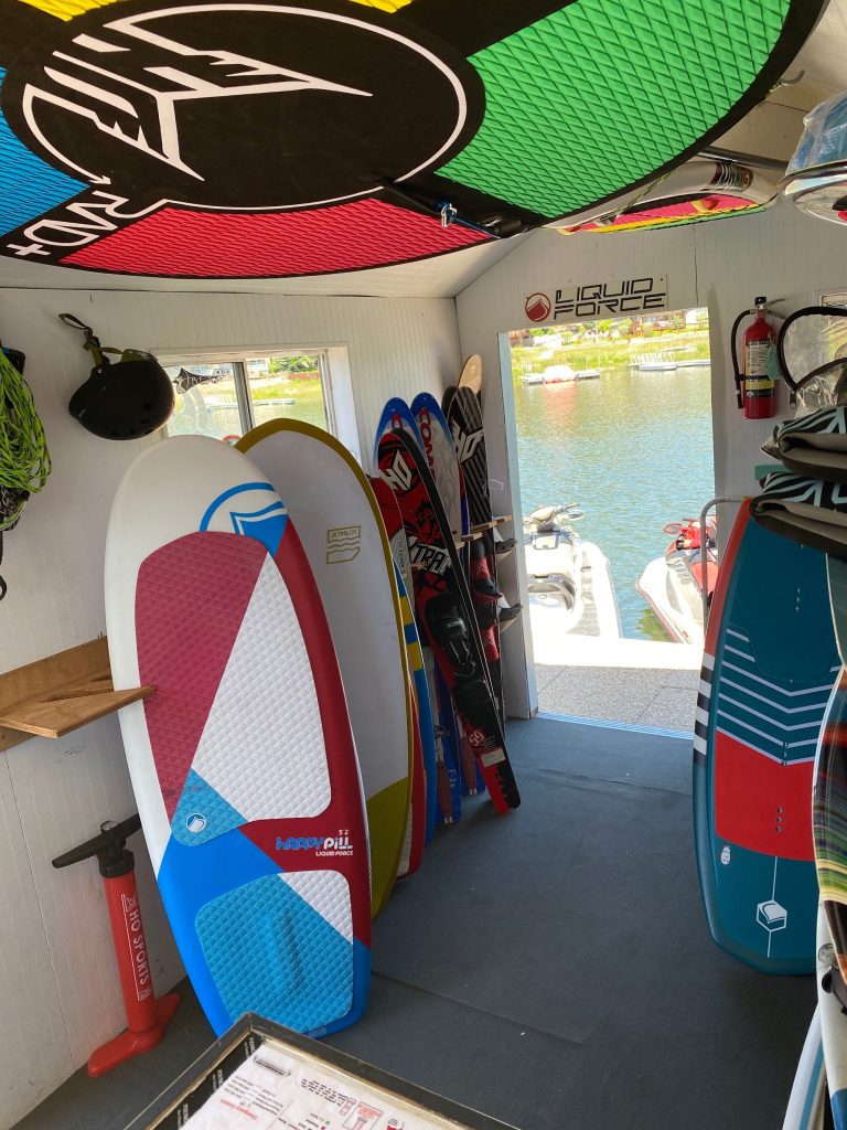 Wakeboards, surfboards, and watersports equipment inside Designated Wakesports rental shop