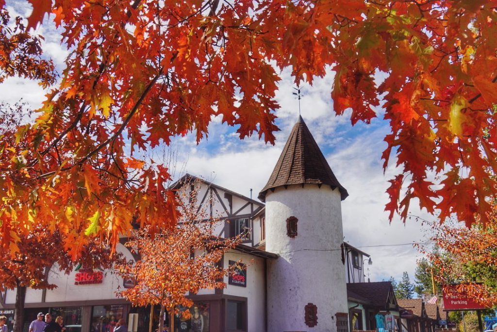 A building with a conical tower is framed by bright orange and red autumn leaves in Big Bear.