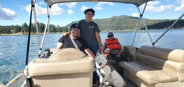 Family enjoying a pontoon boat ride on a lake with their dog on a sunny day.