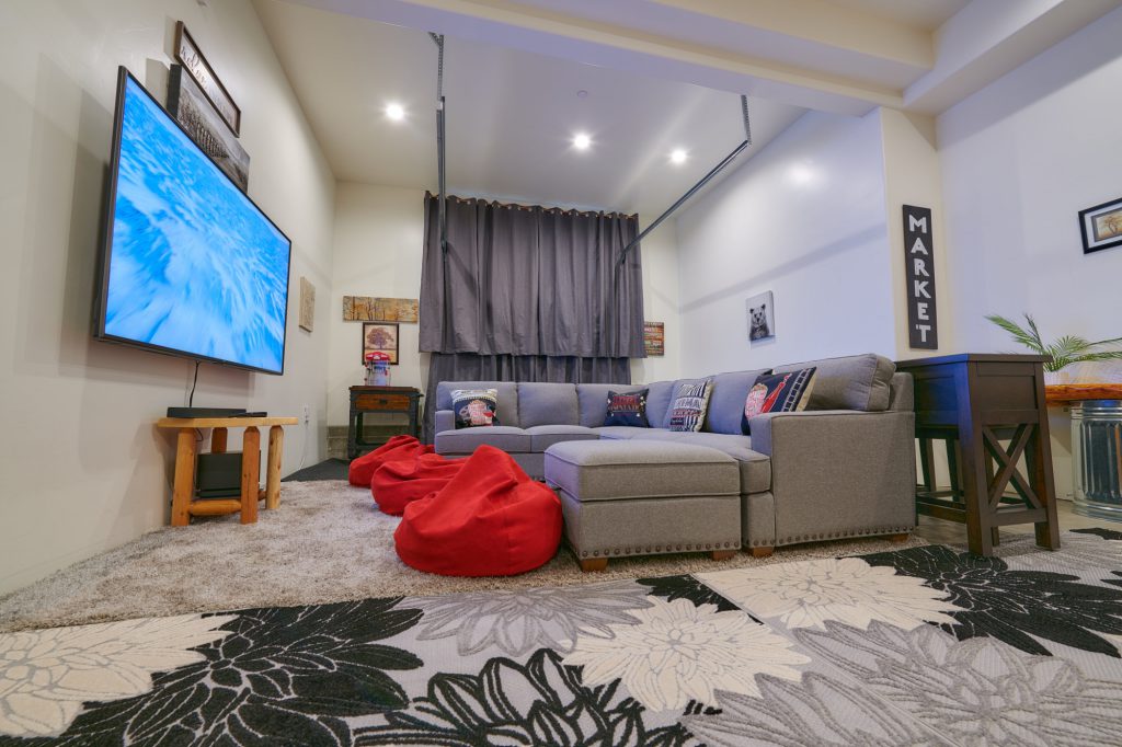 A modern cabin media room in Big Bear with a gray sectional sofa, a large TV, and red beanbag chairs.