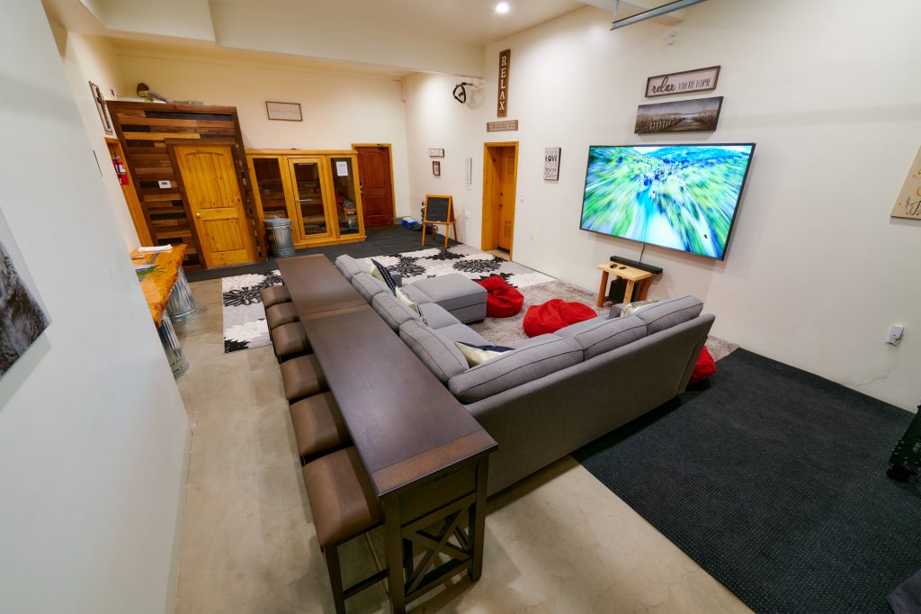 A modern cabin living room in Big Bear with a gray sectional sofa, a long wooden bar with stools, and a TV on the wall.