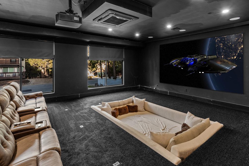 A movie theater room with a large projector screen and a variety of seating options, including a recessed floor pit, in Big Bear.