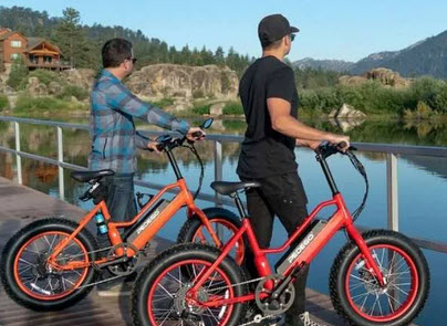 Two men stand on a wooden deck by a lake, looking at the water with their electric bikes at Big Bear.