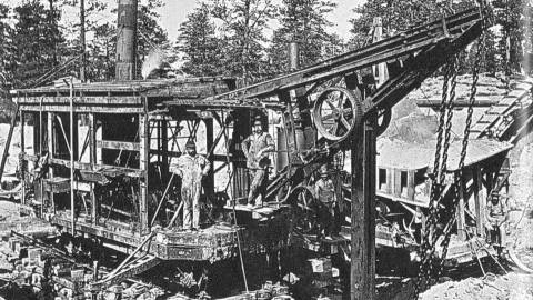 Historic black and white photo of an early gold mining operation in Big Bear with workers and mining equipment.