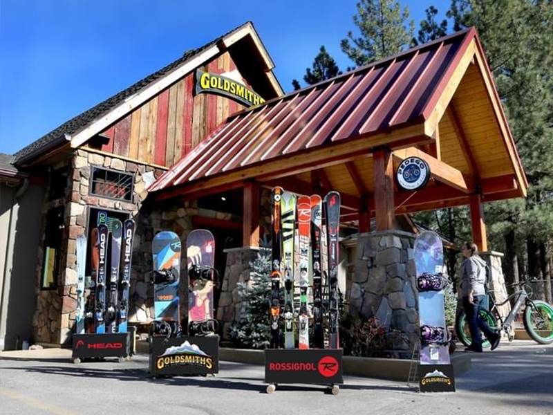 Exterior of Goldsmiths Sports in Big Bear Lake showing skis and snowboards displayed outside the rustic storefront.