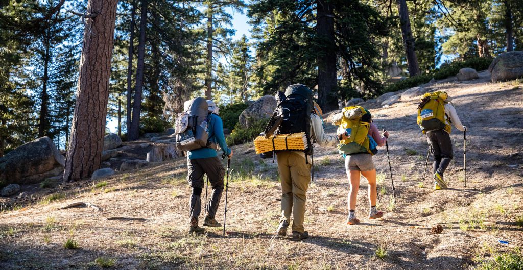 Three hikers with backpacks ascend a trail during the Highlander Adventure in Big Bear.