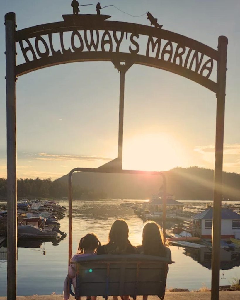 Family sitting on a swing beneath the Holloway’s Marina sign at sunset overlooking Big Bear Lake.