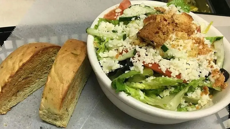 A bowl of fresh salad accompanied by a slice of bread, set against a backdrop featuring a big bear.