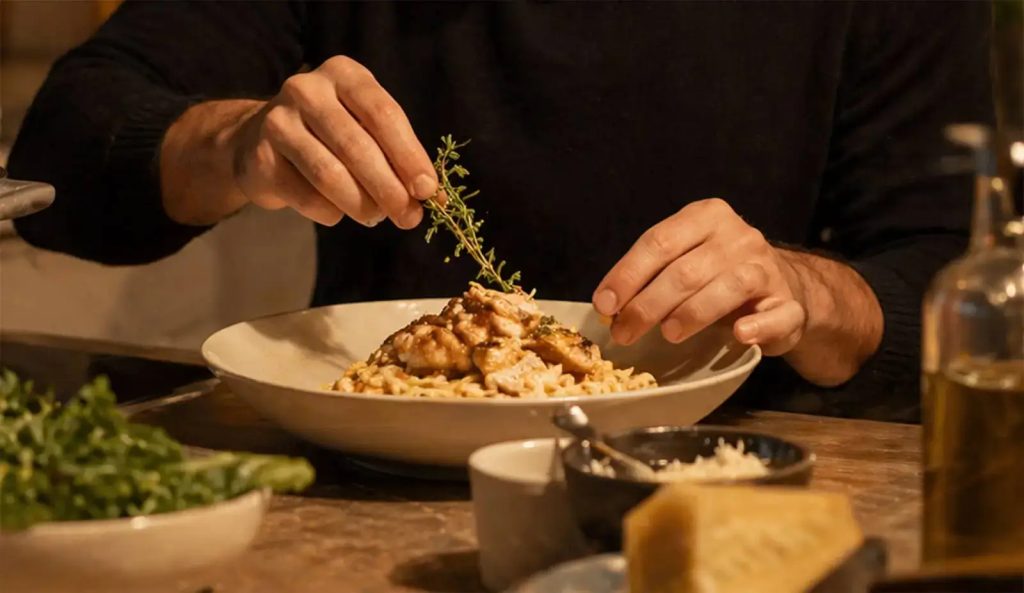 Chef garnishing a freshly prepared gourmet pasta dish with herbs