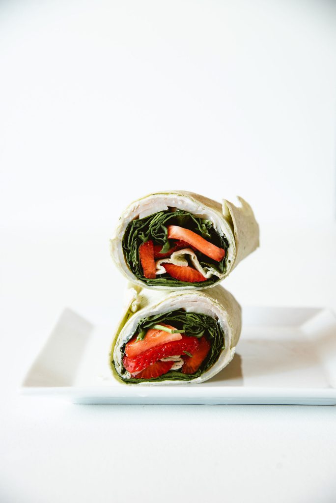 A wrap cut in half and stacked on a white plate, showing a filling of strawberries and greens.