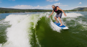 Person wakesurfing behind a boat on Big Bear Lake surrounded by mountain scenery and waves