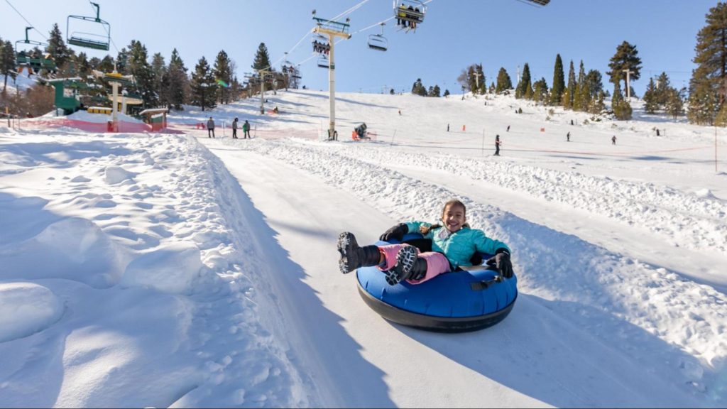 Child enjoying snow tubing at a mountain resort with ski lifts and snowy slopes in the background