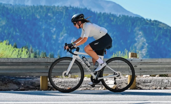Cyclist riding a road bike on a mountain roadway with forested hills in the background
