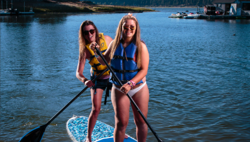 Two friends paddle boarding on Big Bear Lake while enjoying a fun outdoor water activity