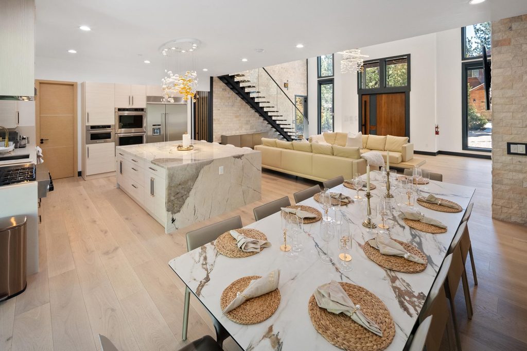 Luxury open-concept kitchen and dining room with marble island, modern staircase, elegant dining table, and spacious contemporary interior design.