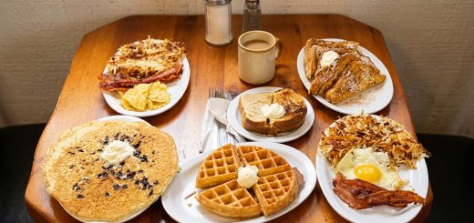 Breakfast spread at Grizzly Manor Cafe in Big Bear Lake featuring pancakes, waffles, French toast, hash browns, eggs, bacon, toast, and coffee on a wooden table.