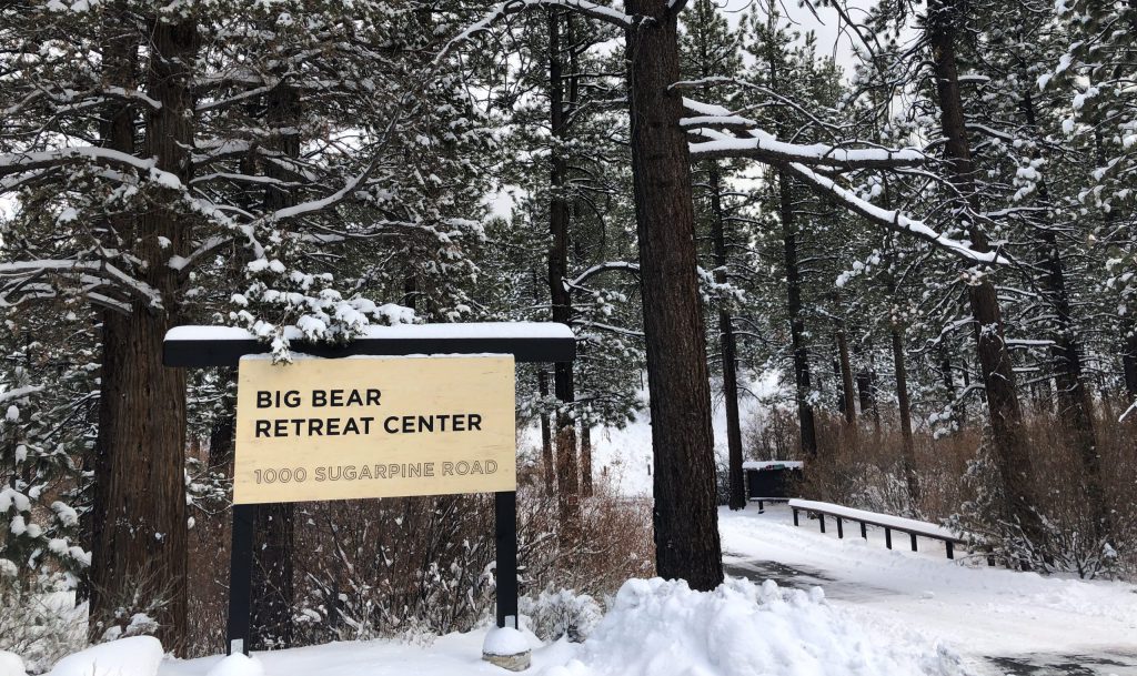 Snow-covered Big Bear Retreat Center surrounded by tall pine trees, showcasing a serene winter landscape.
