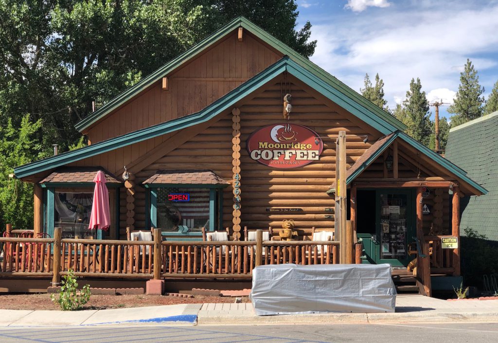The exterior of a log cabin-style building is shown in Big Bear, with a sign that reads "Moonridge Coffee" above the entrance.