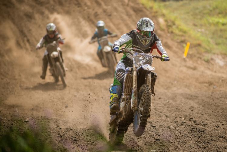 Motocross riders race on a dirt track at Big Bear, with the lead rider kicking up dust and dirt.