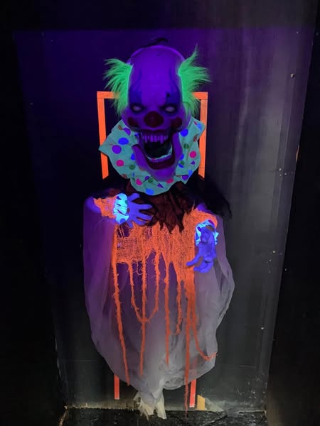 Haunted neon clown prop with glowing eyes inside Mystery Maze attraction