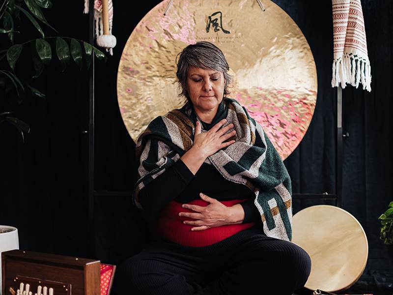A woman sits in front of a large gong at Mystic Rose Studios in Big Bear, creating a serene and meditative atmosphere.