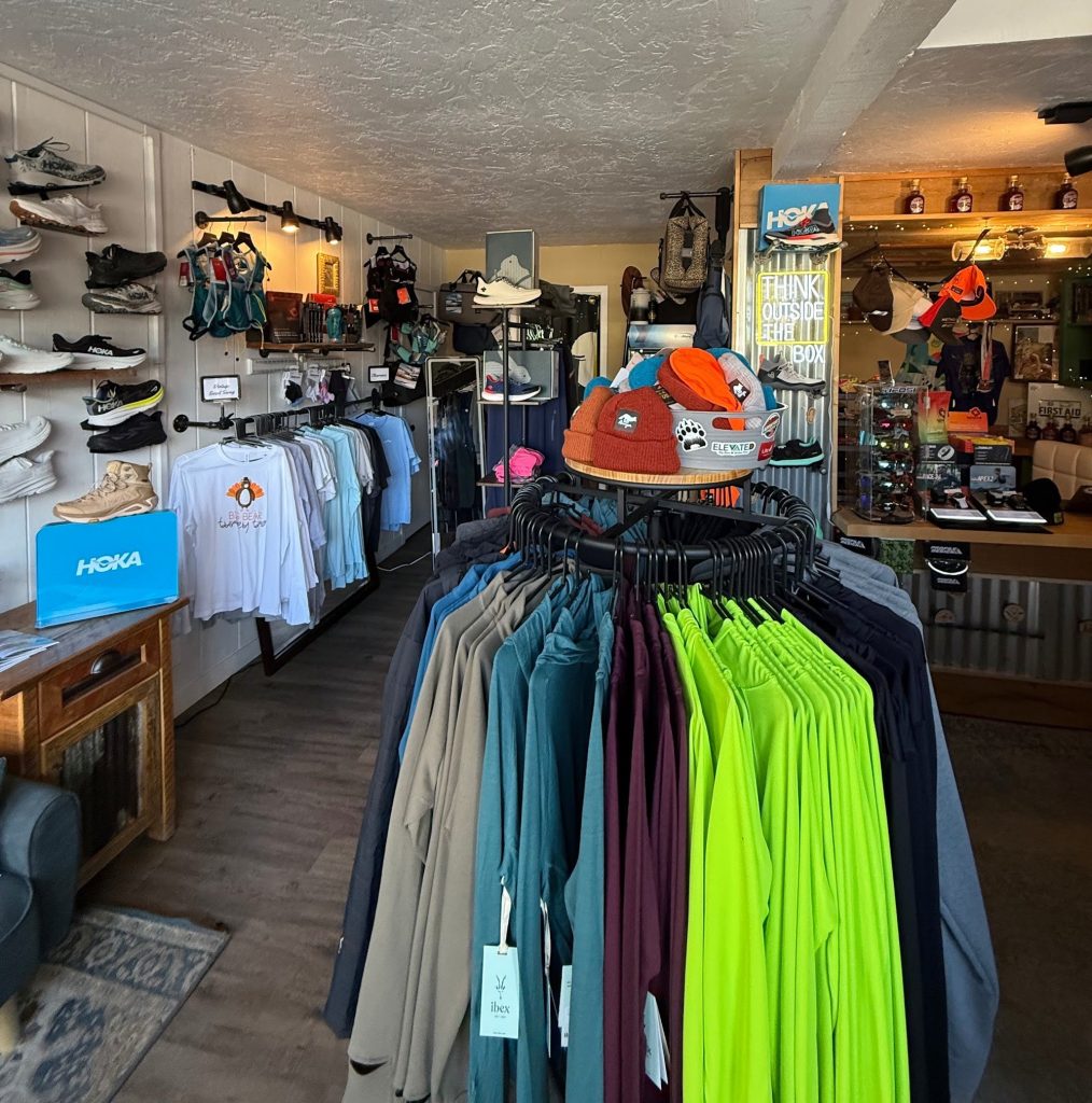 Interior outdoor gear and clothing shop with apparel racks, hats, and accessories on display.