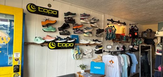 Interior retail wall display of outdoor shoes and footwear with branded sneakers and apparel section inside a store.