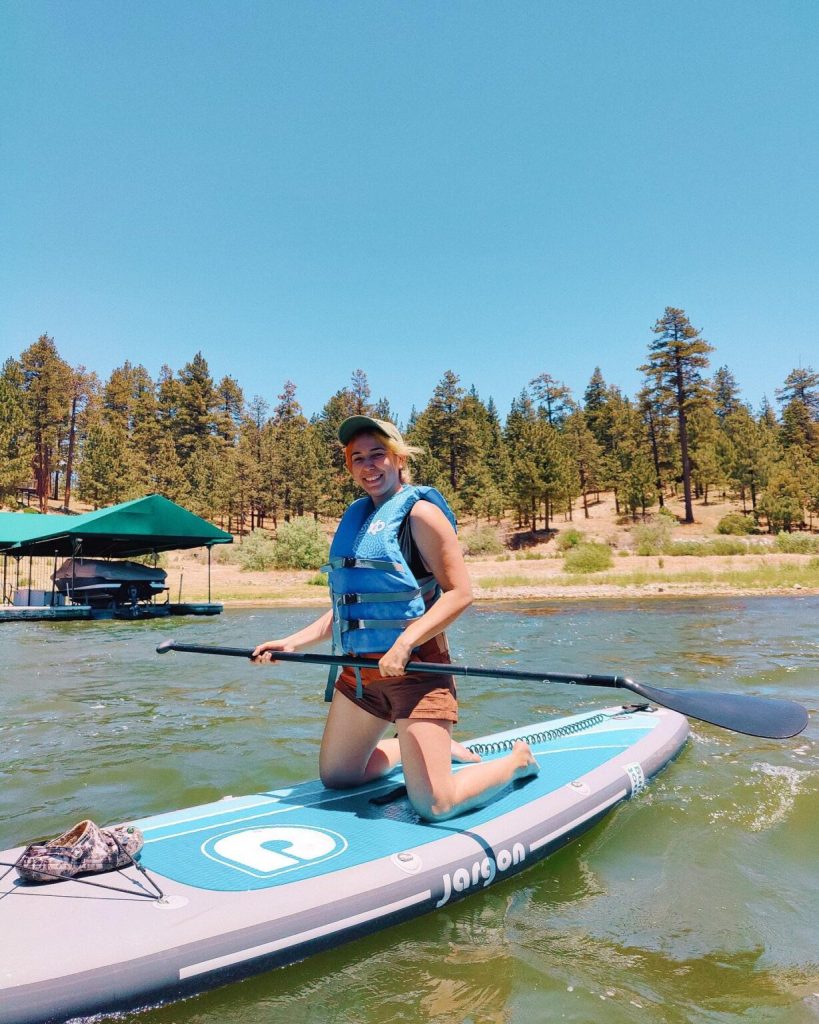 Visitor enjoying stand-up paddleboarding on Big Bear Lake with scenic mountain and forest views.
