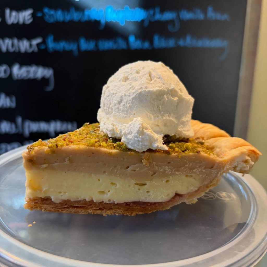 Close‑up slice of creamy pie with pistachio topping and whipped cream