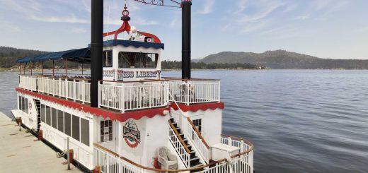 A riverboat docked at Pine Knot Marina, with another boat resting on top, set against the backdrop of Big Bear.
