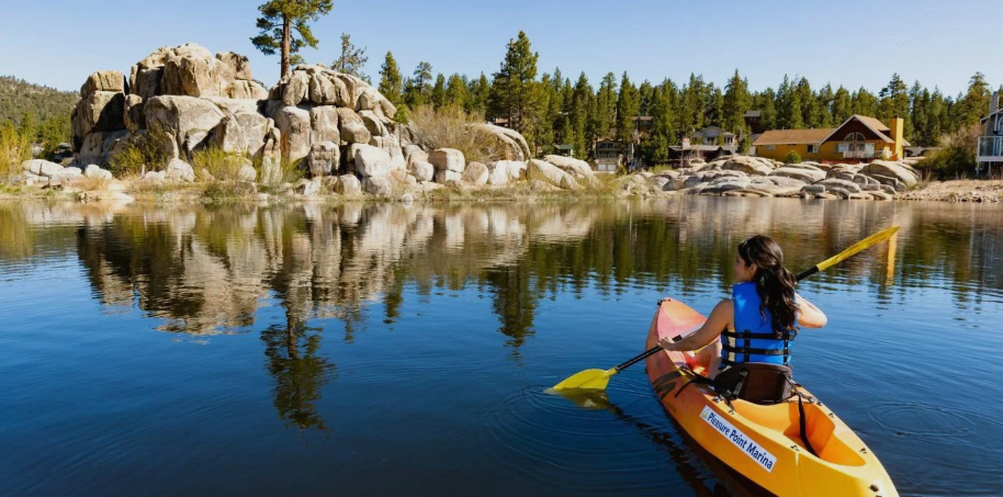 Person kayaking on a calm lake near rocky shoreline with mountain reflections and scenic outdoor landscape