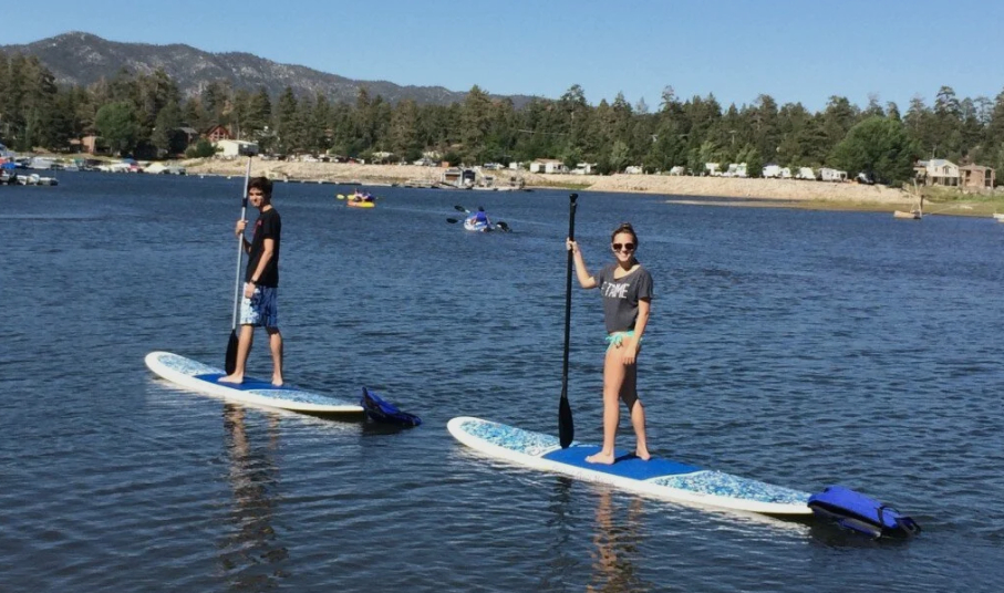 Two people stand-up paddleboarding on a calm mountain lake with scenic shoreline and distant forested hills