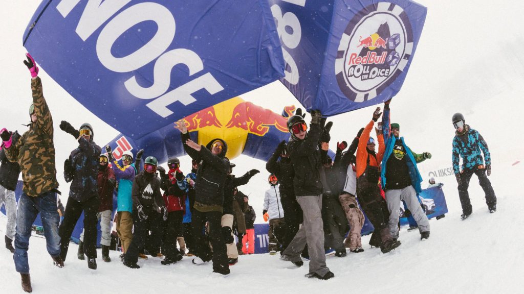 Snowboarders celebrating under a giant Red Bull Roll the Dice inflatable dice at Bear Mountain during a snowy event in Big Bear.