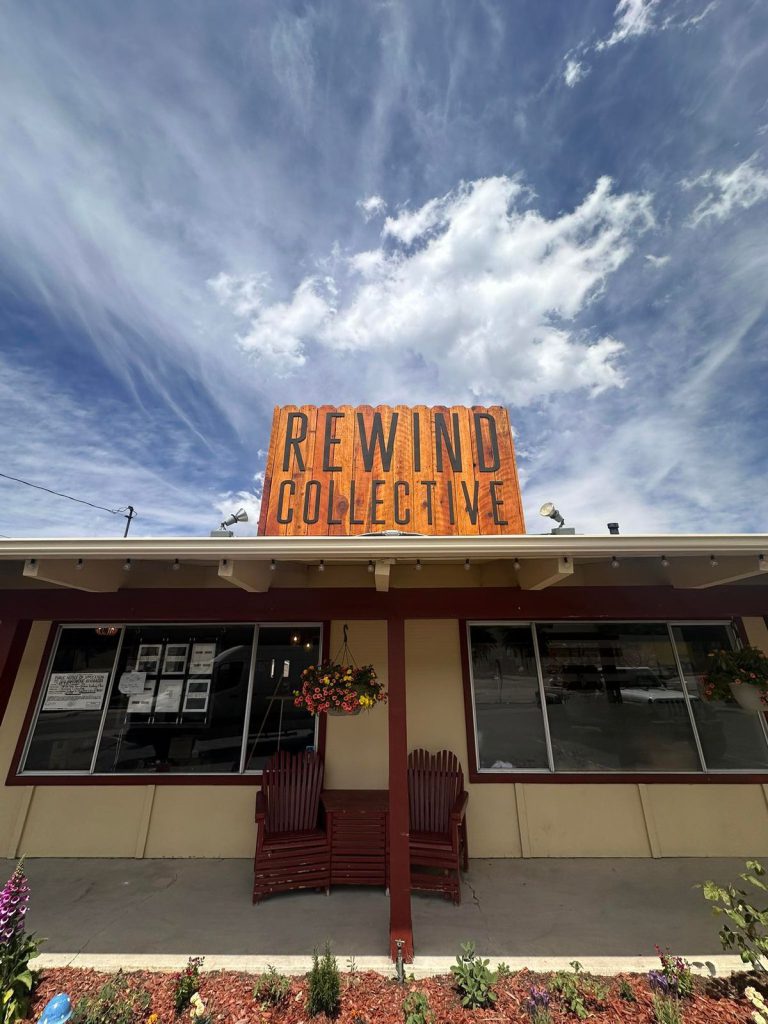 The storefront of Rewind Collective in Big Bear, with a wooden sign on the roof and a wide-angle view of the building against a cloudy blue sky.