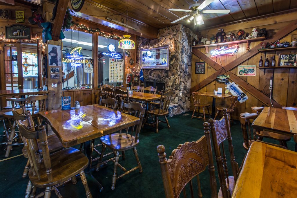Rustic dining room with wooden tables, stone fireplace, and neon beer signs inside a Big Bear Mountain Brewery